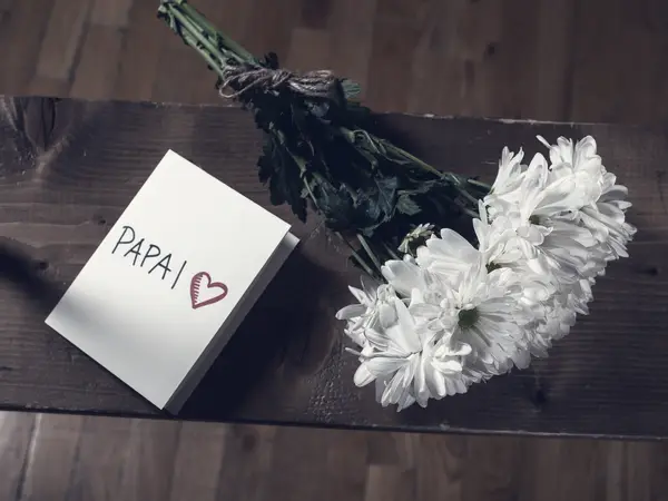 A handwritten greeting card lying next to a bunch of white flowers on a wooden table